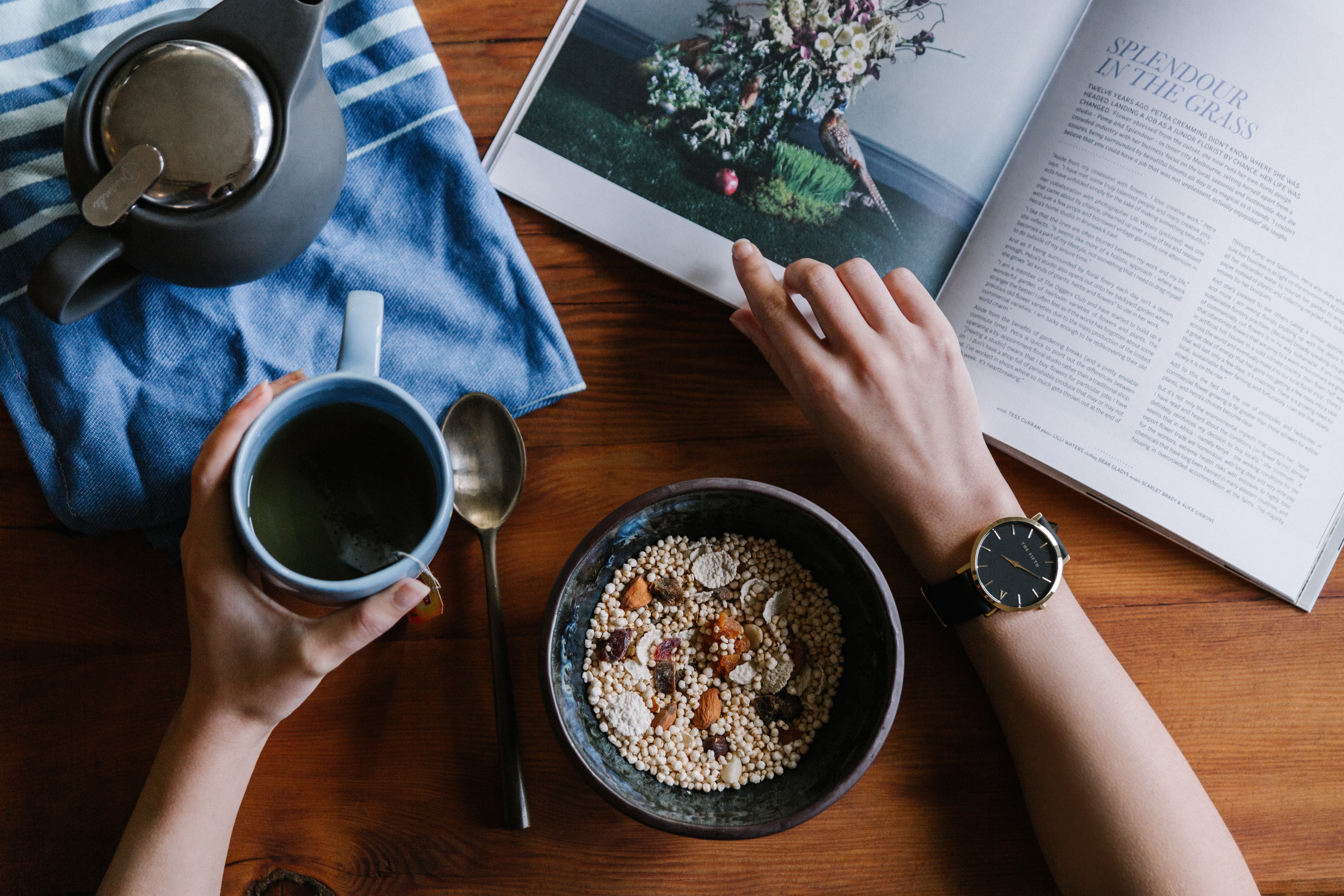 A person eating breakfast, drinking coffee and reading a magazine